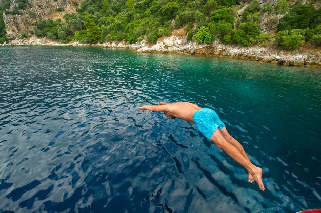 Um homem de short azul mergulha de um navio no mar perto da costa