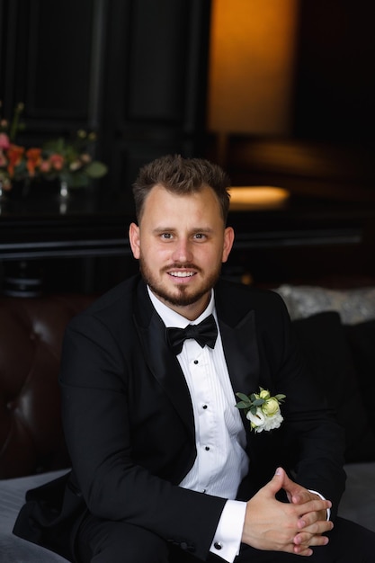 Um homem de smoking está sentado em frente a uma mesa com flores.