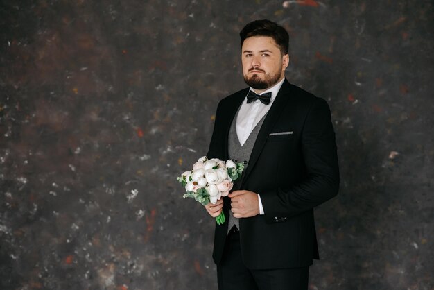 Foto um homem de smoking segura um buquê de flores.