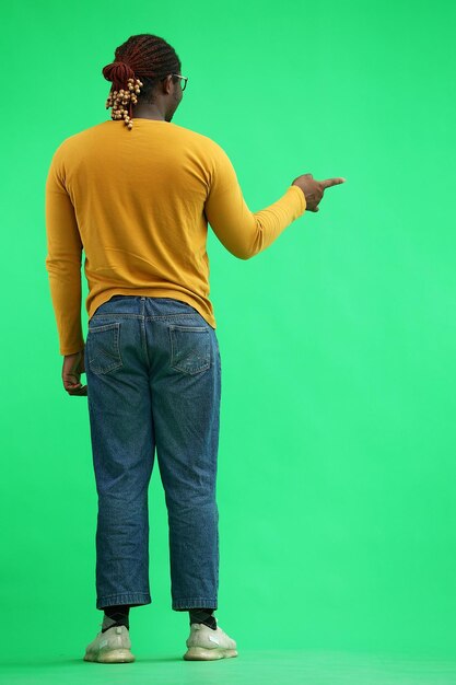 Um homem de suéter amarelo aponta para o lado em uma vista traseira de fundo verde