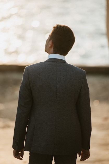 Um homem de terno cinza posa na rua para anunciar roupas masculinas. Tiro para loja de roupas masculinas