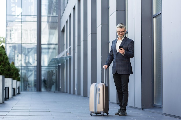 Um homem de terno com uma grande mala de viagem e um telefone está digitando uma mensagem e reservando um