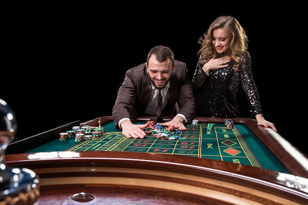 Um homem de terno com uma mulher em um lindo vestido preto jogando roleta no cassino. Jogos de azar. Casino. Roleta. Pôquer.