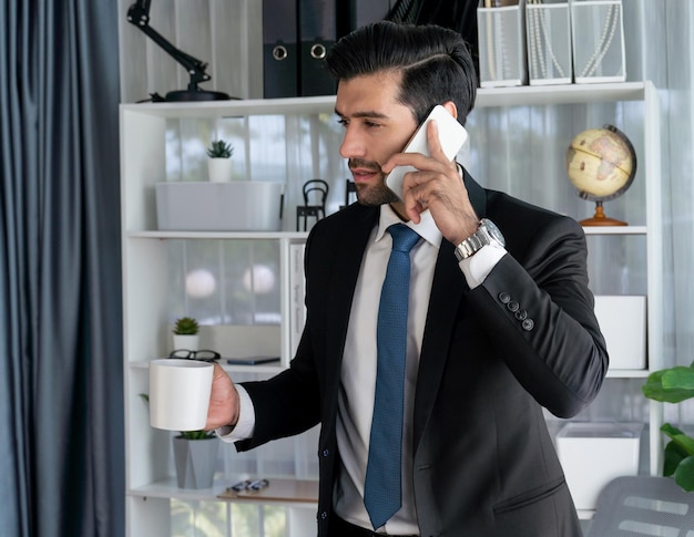 Um homem de terno está falando ao telefone e segurando uma caneca de café.