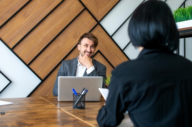Um homem de terno está sentado em seu local de trabalho e rindo com colegas