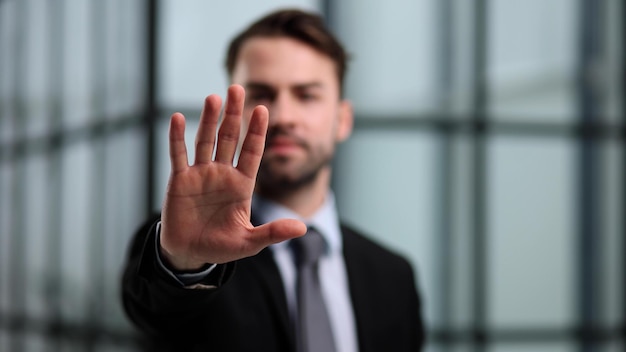 Um homem de terno preto e camisa branca mostrando segurar ou parar o gesto com a mão