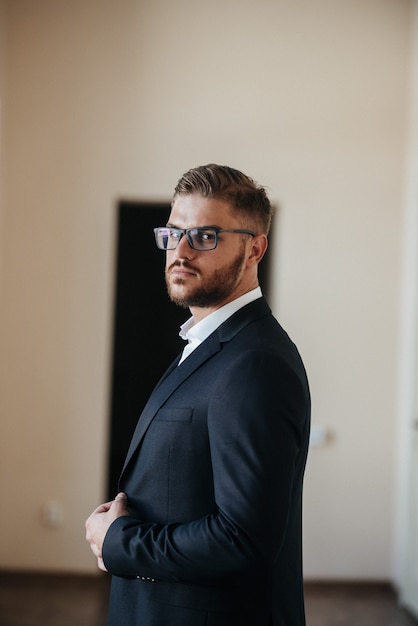 Um homem de terno preto e camisa branca posa dentro de casa para anunciar roupas masculinas. Tiro para loja de roupas masculinas