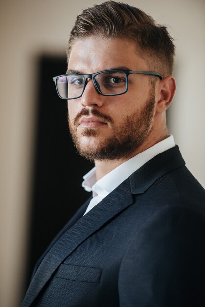 Um homem de terno preto e camisa branca posa dentro de casa para anunciar roupas masculinas. Tiro para loja de roupas masculinas