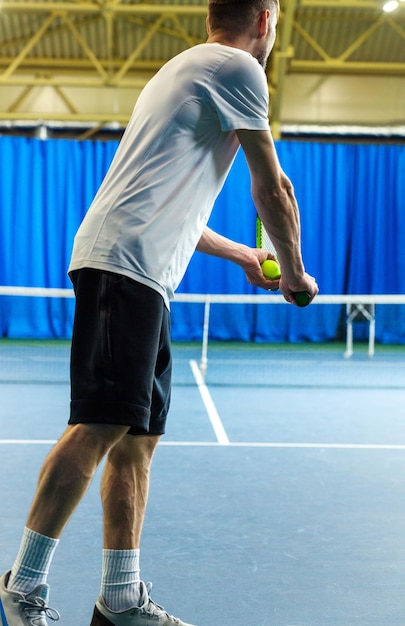 Um homem de uniforme esportivo fica de costas para a câmera segurando uma raquete e uma bola nas mãos e está prestes a servir Foto vertical