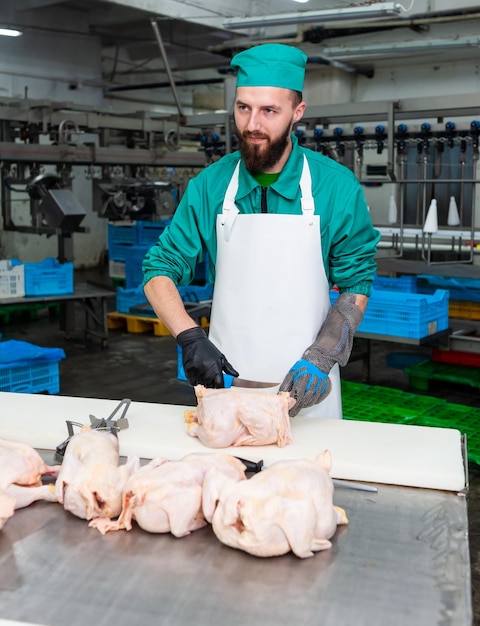 Um homem de uniforme verde corta frango em uma mesa