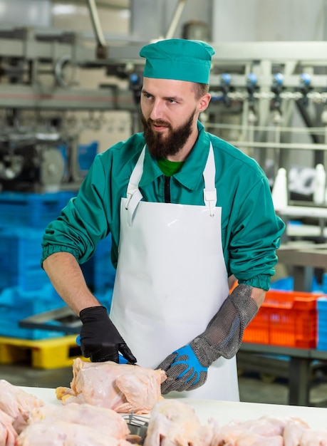 Foto um homem de uniforme verde está cortando carne em uma fábrica.
