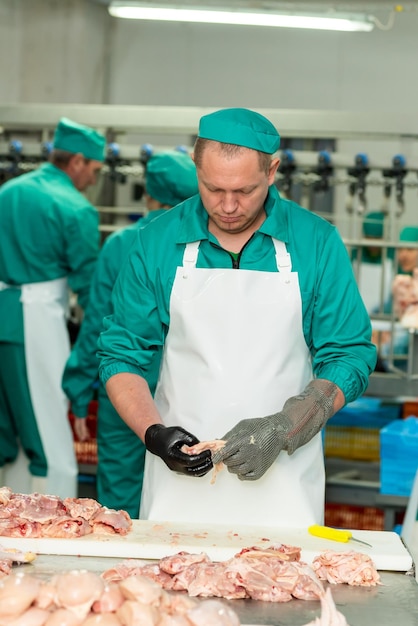 Um homem de uniforme verde está cortando carne em uma fábrica.
