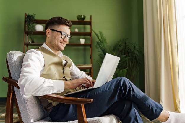 Um homem de vestuário casual elegante está focado em seu laptop confortavelmente sentado em uma cadeira vintage