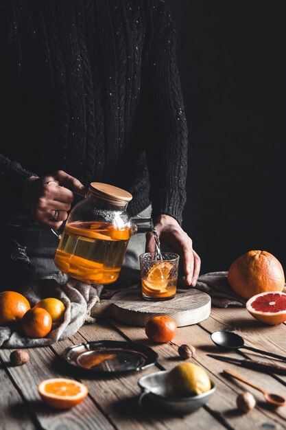 Um homem derrama chá de frutas cítricas em uma mesa de madeira. Bebida saudável, estilo vintage. Produtos ecológicos e veganos.