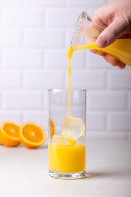 Um homem derrama suco de laranja de uma garrafa em um copo alto com gelo O conceito de frescura e utilidade Ao fundo está uma laranja cortada ao meio Foco seletivo closeup fundo branco