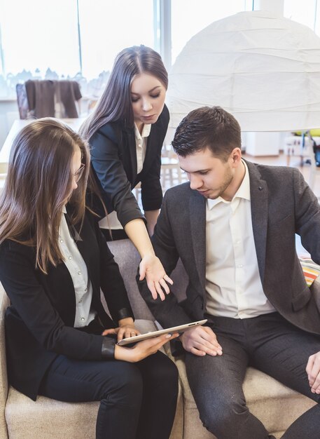 Um homem e duas mulheres de jaquetas estão discutindo o trabalho em uma reunião de negócios. eles estão olhando para o tablet