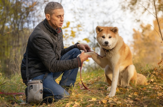 Um homem e seu cachorro Akita Inu na floresta de outono