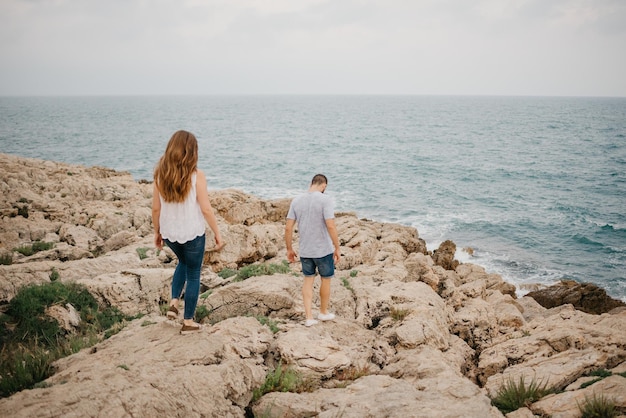 Um homem e sua namorada estão descendo da colina rochosa para o mar na Espanha