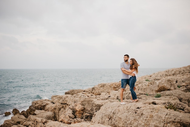 Um homem e sua namorada estão se abraçando na costa rochosa do mar na Espanha