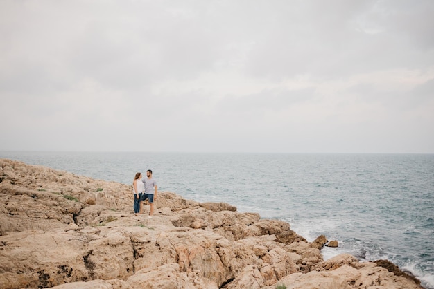 Um homem e sua namorada estão se abraçando na costa rochosa do mar na Espanha