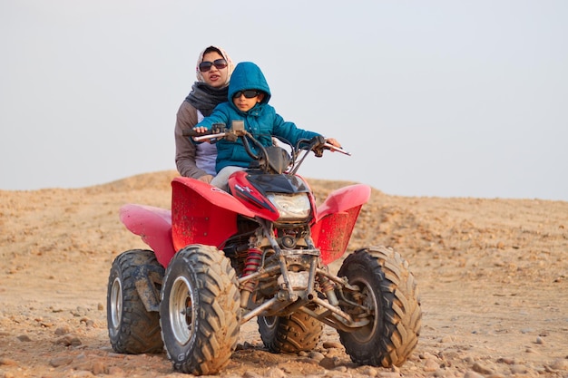 Um homem e um menino andam de quadriciclo no deserto.