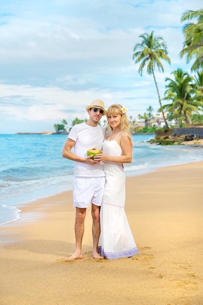 Um homem e uma garota na praia estão bebendo coco.