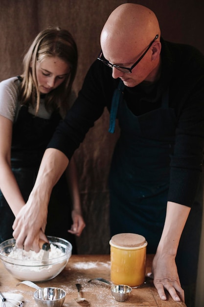 Um homem e uma jovem misturando ingredientes em uma tigela de vidro em uma mesa de cozinha