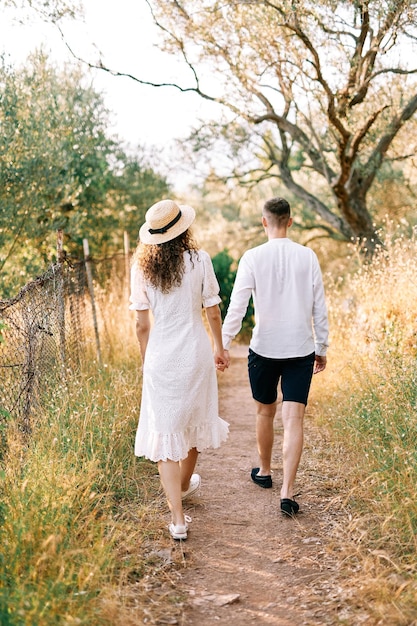 Foto um homem e uma menina caminham ao longo de uma estrada de campo em um bosque segurando as mãos para trás