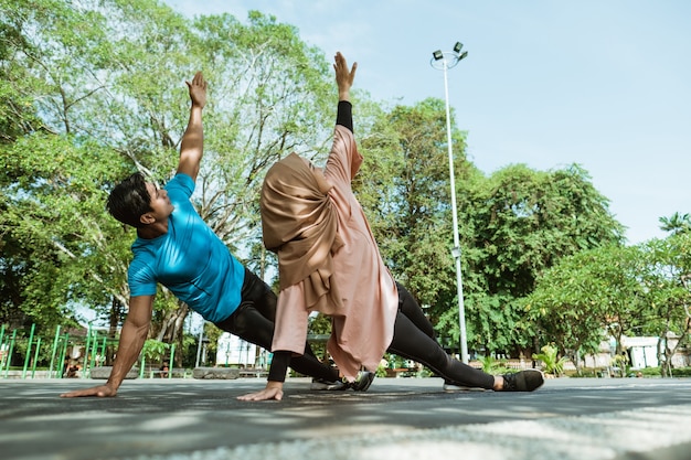 Um homem e uma menina com um véu em roupas de ginástica, fazendo exercícios de mão juntos para treinamento de resistência no parque