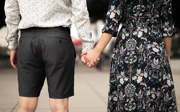 Um homem e uma mulher de mãos dadas, ambos de bermuda e camisa florida.