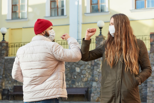 Um homem e uma mulher de máscaras batem nos cotovelos em vez de cumprimentar com um aperto de mão