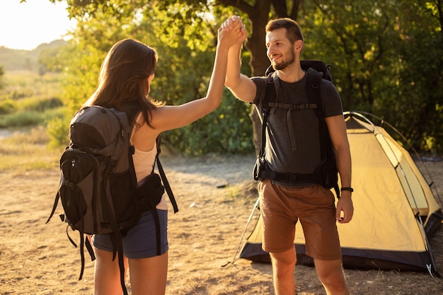 Um homem e uma mulher em uma caminhada com mochilas perto de uma tenda ao pôr do sol, olá cinco. Lua de mel na natureza