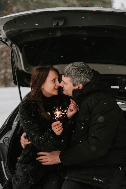 Um homem e uma mulher no fundo de uma floresta coberta de neve em uma nevasca no porta-malas de um carro