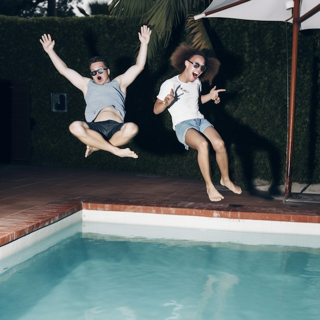 Foto um homem e uma mulher pulando em uma piscina com um usando óculos escuros e o outro usando óculos escuros.