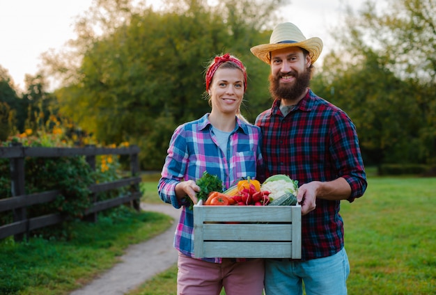 Um homem e uma mulher segurando uma caixa com uma colheita de legumes da fazenda