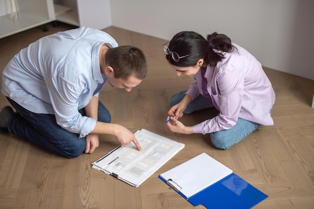 Um homem e uma mulher sentados no chão e olhando a planta de um novo apartamento nos desenhos