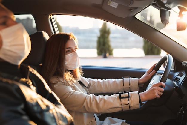 Um homem e uma mulher usando máscaras médicas e luvas de borracha para se protegerem de bactérias e vírus enquanto dirigem um carro. a mulher ao volante. coronavírus (covid-19