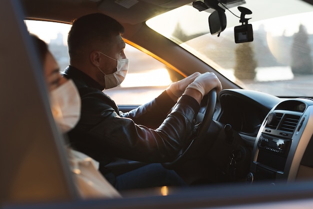 Um homem e uma mulher usando máscaras médicas e luvas de borracha para se protegerem de bactérias e vírus enquanto dirigem um carro. homens mascarados no carro. coronavírus (COVID-19