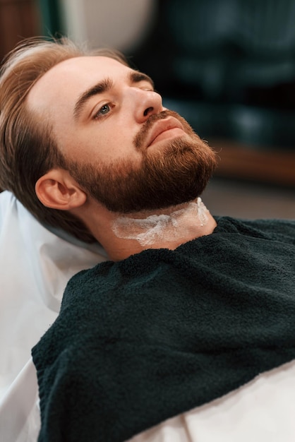 Um homem elegante com barba e creme no pescoço está na barbearia.