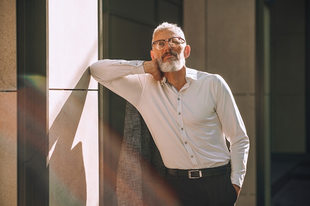 Foto um homem elegante de cabelos grisalhos em pé perto da parede, perto do prédio de escritórios