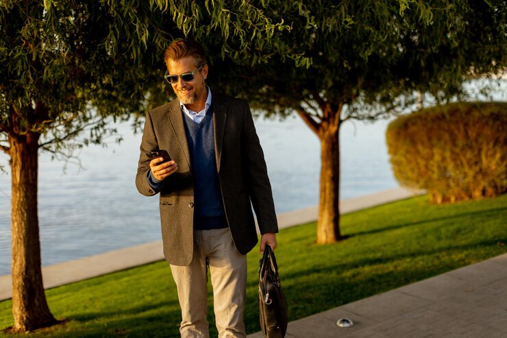 Foto um homem elegante desfruta de um passeio tranquilo ao longo da beira-mar conversando em seu telefone em meio à folhagem de outono na luz dourada da tarde