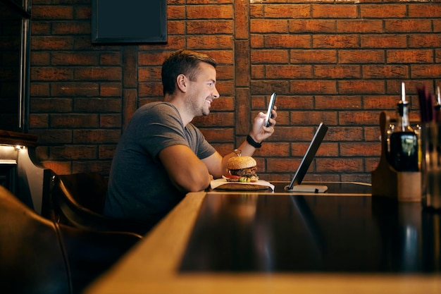 Um homem elegante está sentado em um restaurante em uma pausa de almoço e sorrindo para seu telefone