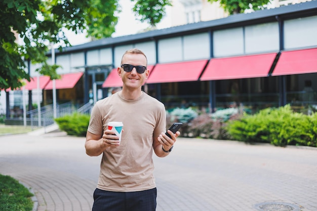 Um homem elegante sorridente barbudo de camisa branca e óculos de sol nas ruas da cidade e ligando no celular