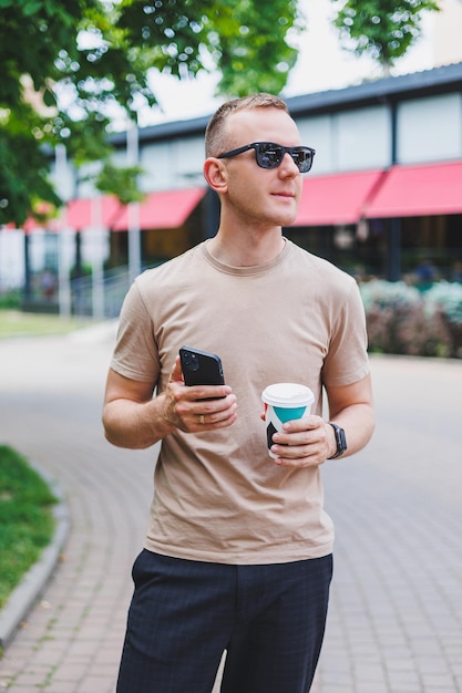 Um homem elegante sorridente barbudo de camisa branca e óculos de sol nas ruas da cidade e ligando no celular