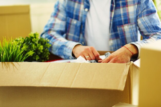 Um homem em movimento sentado no chão em um apartamento vazio entre as caixas verificando a lista de coisas