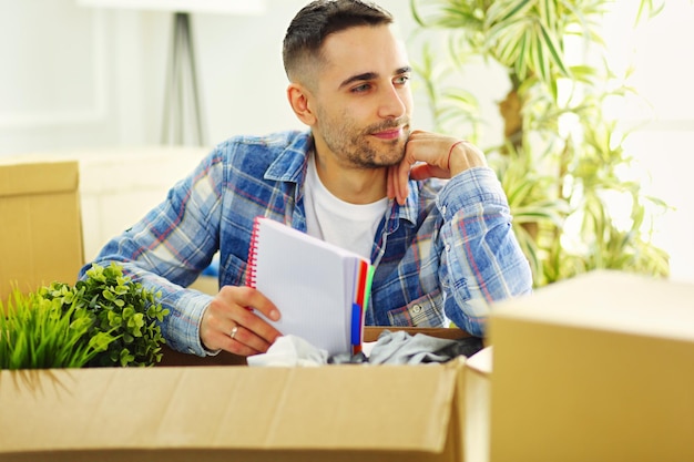 Um homem em movimento sentado no chão em um apartamento vazio entre as caixas verificando a lista de coisas