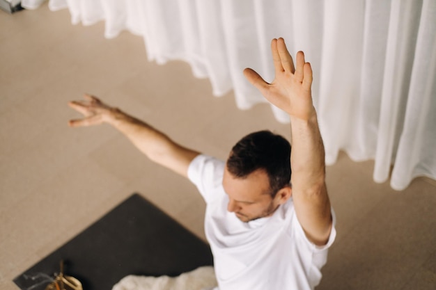 Um homem em roupas esportivas brancas está fazendo ioga com uma sala de ginástica o conceito de um estilo de vida saudável