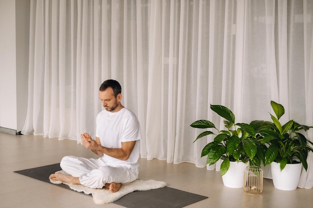 Um homem em roupas esportivas brancas está fazendo ioga com uma sala de ginástica o conceito de um estilo de vida saudável