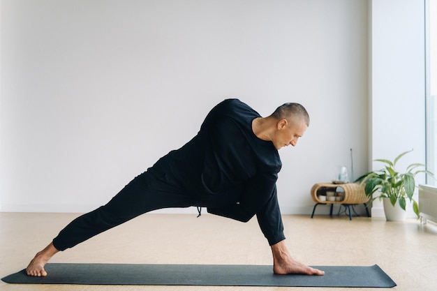 Um homem em roupas esportivas pretas está fazendo Yoga se alongando na academia