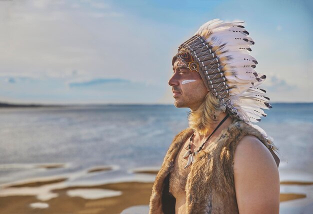 Um homem em roupas tradicionais nativas americanas perto do mar